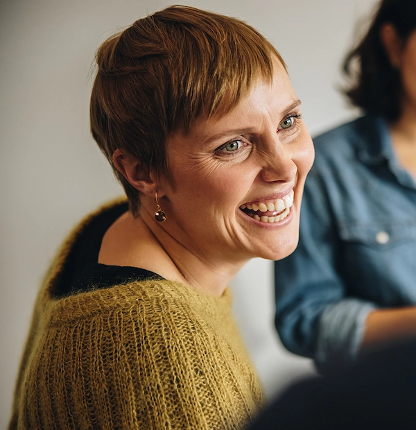 Lachende vrouw met kort haar in gesprek met collega’s op kantoor.